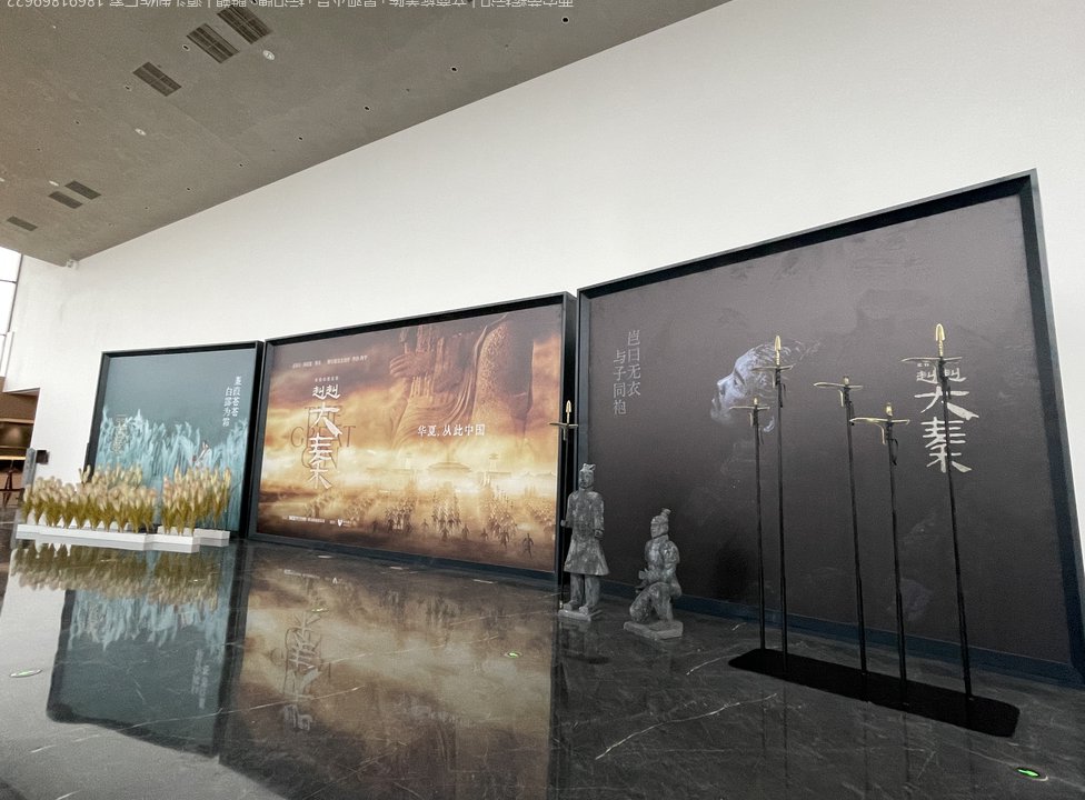 剧场室内多块大型灯箱并排展示，配秦俑造型与兵器展架造景