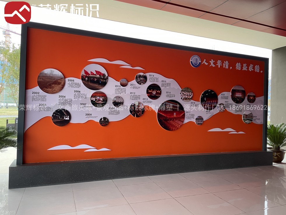 周至华清学院室内文化墙现场实景,橙色底板上白色飘带作时间轴串联校史照片与校徽标语