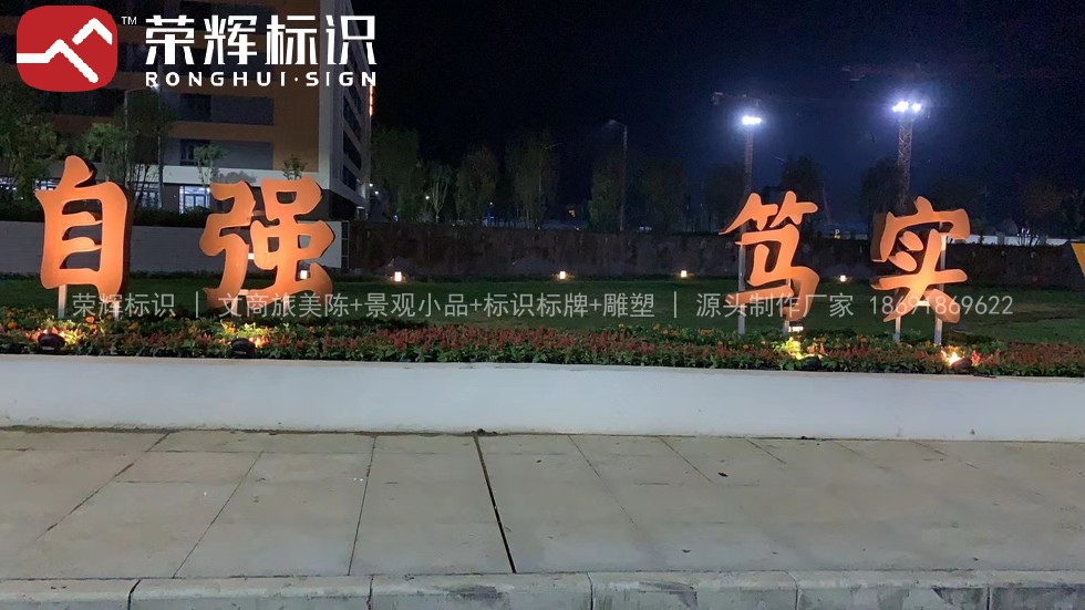 周至华清学院夜间景观字现场实景,草坪上橙色发光立体字自强笃实经金属支架固定在低矮基座上