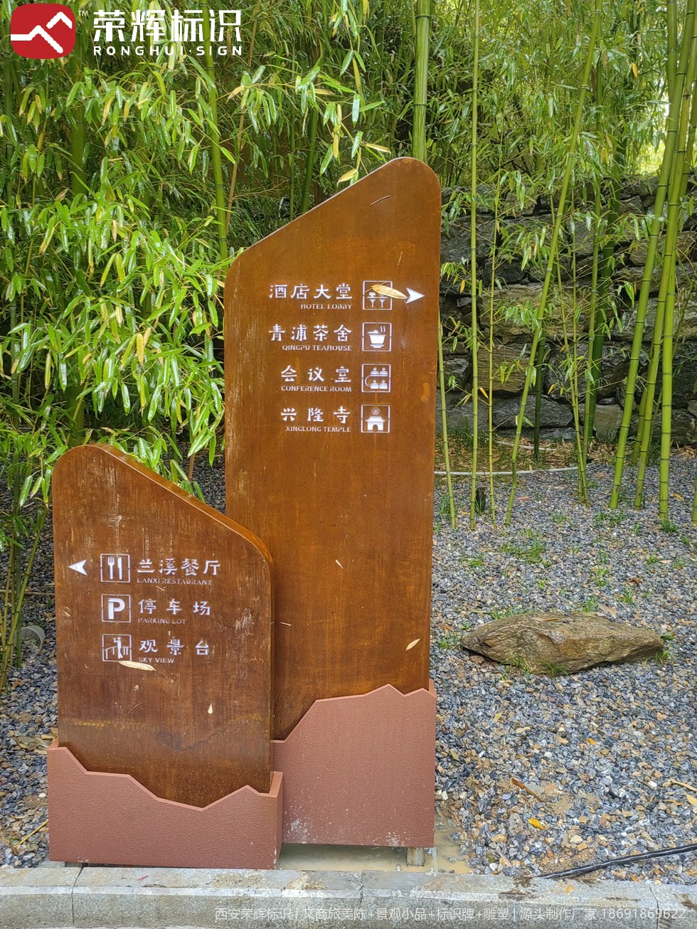 镇安合曼兰若度假酒店庭院石景前的落地式耐候钢导视立牌,锈色面板配白色图文指示园区方向