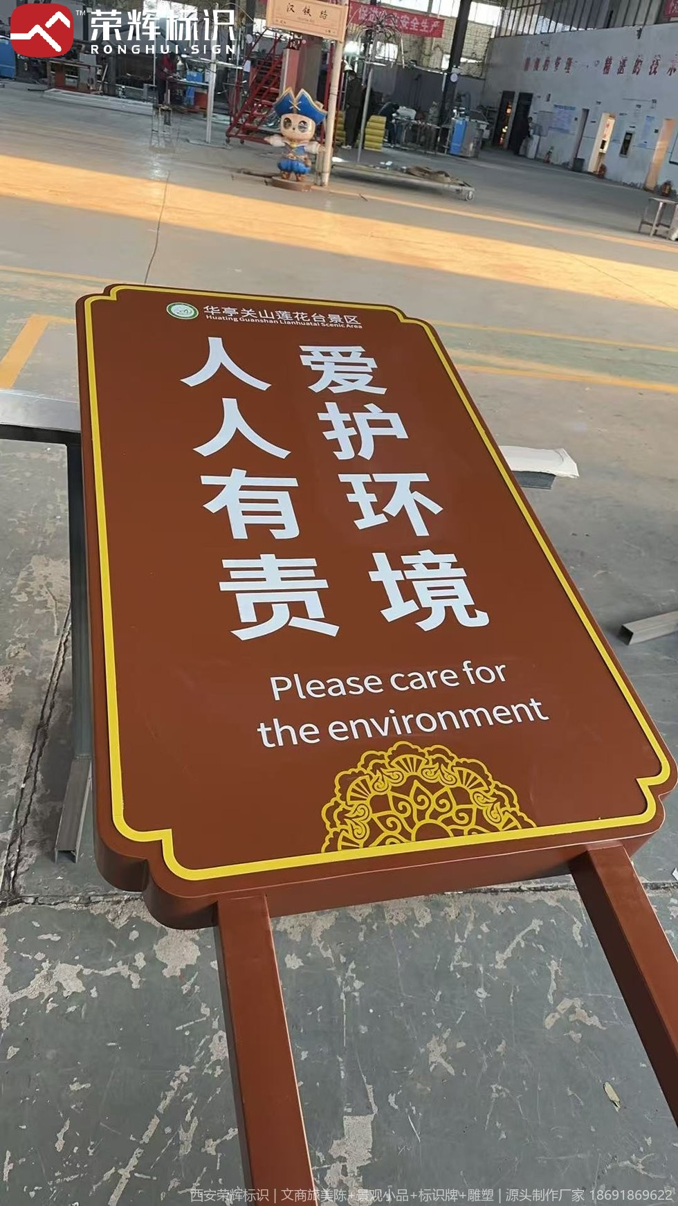 标识车间内平放的立式环保提示牌,深棕底色配金色描边与莲花纹浮雕,牌面为竖排白色中文字与英文提示语