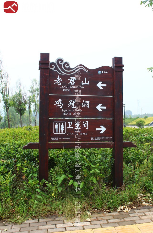老君山景区道路弯道处双立柱指路牌现场实景,深红褐仿木面板分栏指向景区与溶洞景点及卫生间