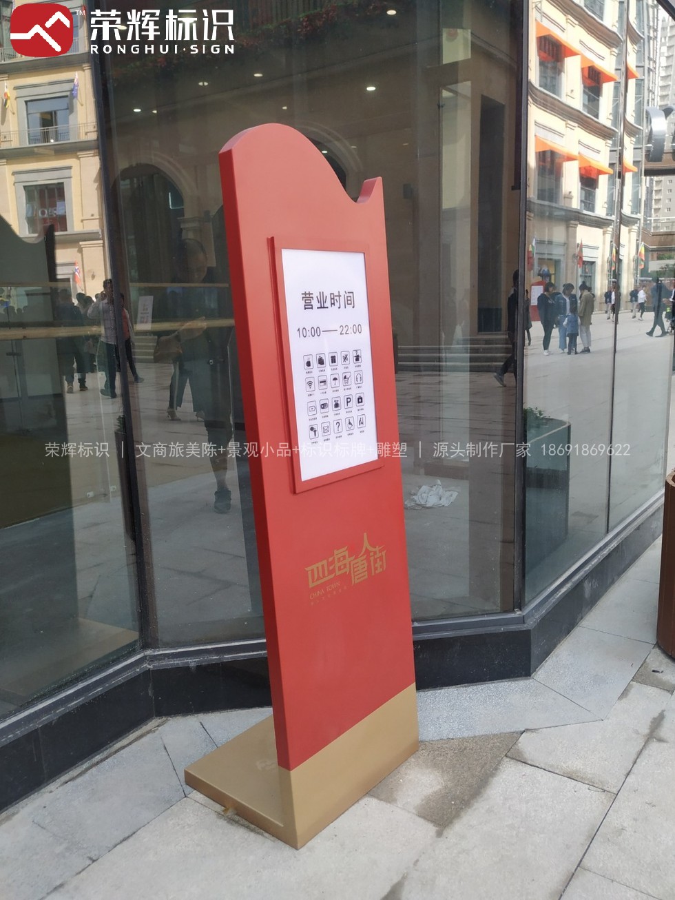 商业街区内的落地式营业时间牌实拍,珊瑚红主体配金色底座,白色面板标注营业时间与图示服务说明